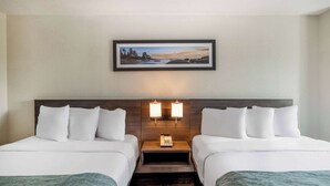 A hotel room with two beds, a nightstand with a phone, wall-mounted lamps, and a framed picture above the beds.