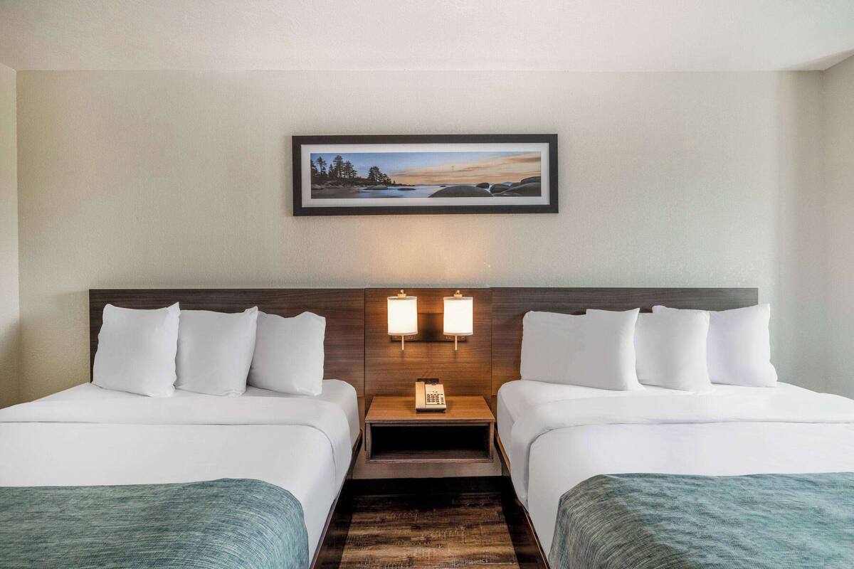 A hotel room with two beds, a nightstand with a phone, wall-mounted lamps, and a framed picture above the beds.