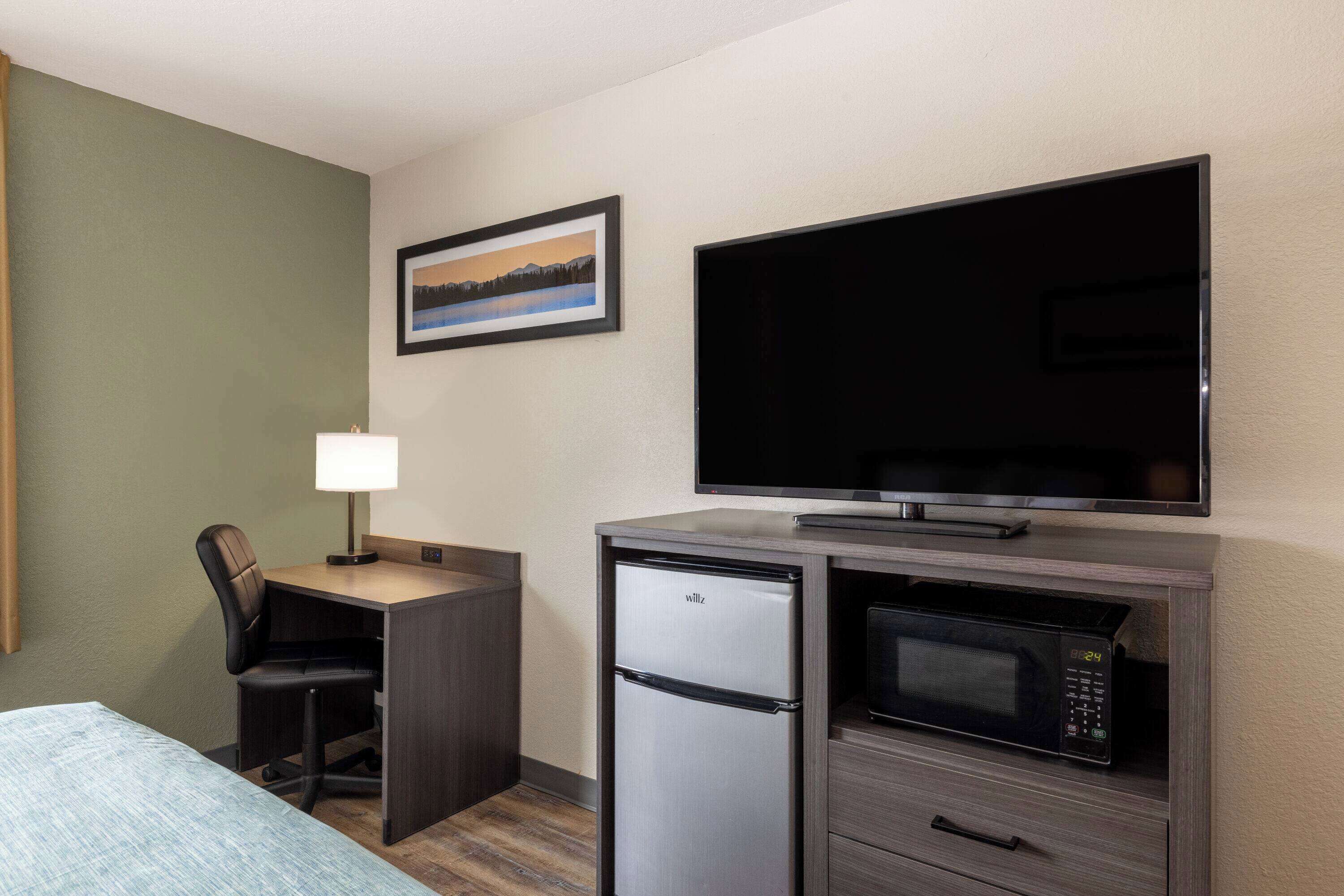 Ein Hotelzimmer mit Bett, Schreibtisch mit Stuhl, Kühlschrank, Mikrowelle und einem Flachbildfernseher.