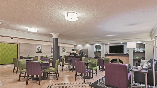 A spacious dining area with multiple tables and chairs, a patterned rug, and a seating area with a couch and side table. - Travelodge by Wyndham Houston Cy-Fair (Houston)