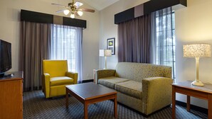 A hotel room with a yellow armchair, a patterned sofa, a wooden table, a ceiling fan, and a lamp. - Travelodge by Wyndham Houston Cy-Fair (Houston)