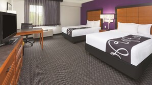 A hotel room with two beds, a desk with a computer, a TV, and a window with curtains. - Travelodge by Wyndham Houston Cy-Fair (Houston)