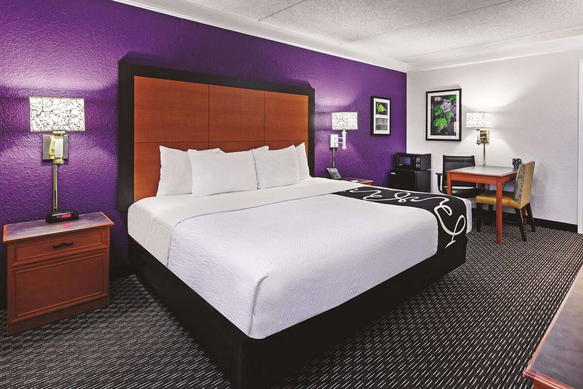 Habitación de hotel con una cama grande, un escritorio con silla, una lámpara de escritorio, un teléfono y cuadros en la pared.