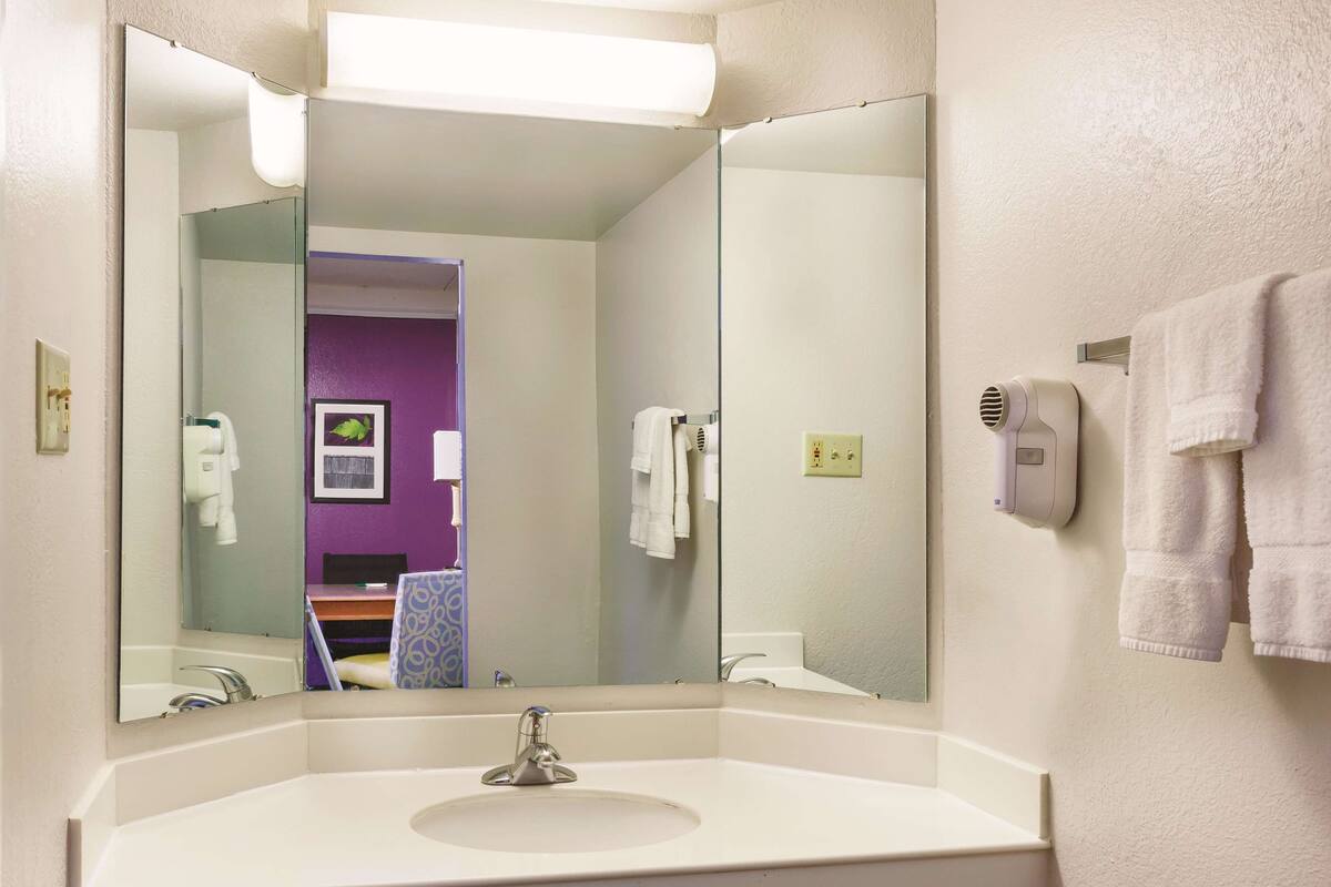 Un baño con un espejo grande, un lavabo, un perchero para toallas y un secador de manos.