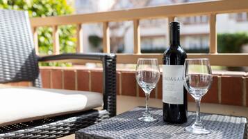 A wicker chair with a cushion, a bottle of wine, and two glasses on a table.