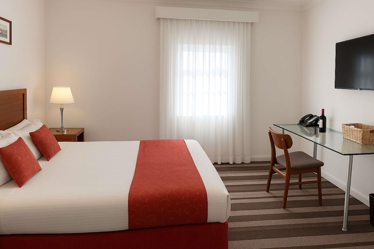 A hotel room with a bed, a desk, a chair, a TV, and a window with curtains.
