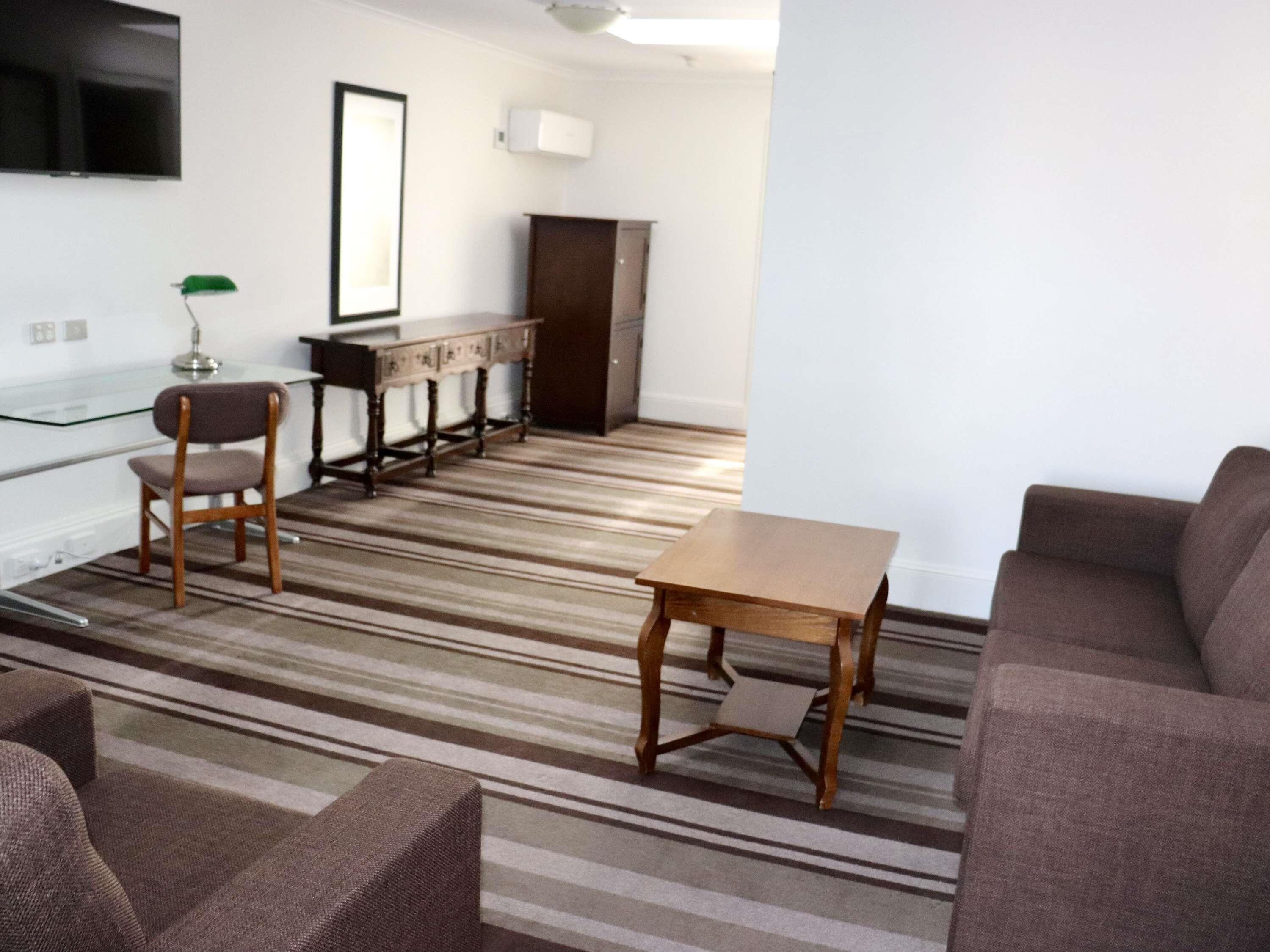 A living room with a striped carpet, a wooden coffee table, a sofa, and a TV mounted on the wall.