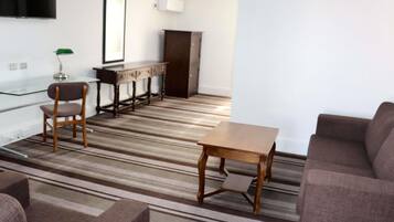A living room with a striped carpet, a wooden coffee table, a sofa, and a TV mounted on the wall.