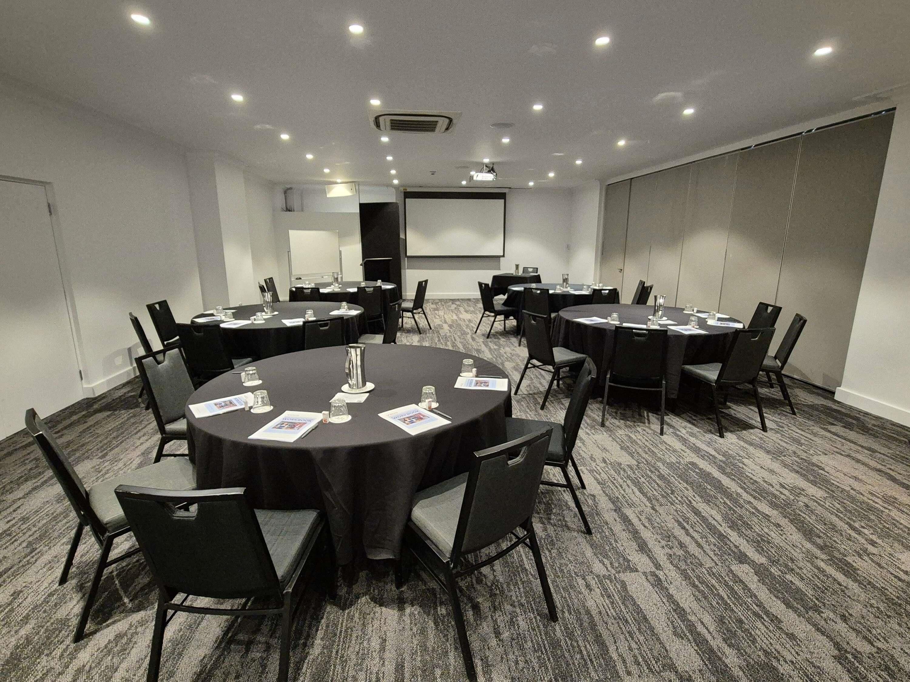 Een congrescentrum met ronde tafels, stoelen en een projectiescherm.