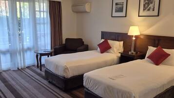 A hotel room with two beds, a chair, a small table, and a lamp.