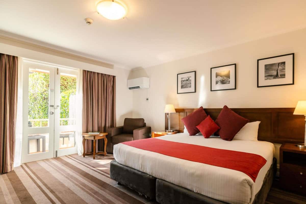 A hotel room with a large bed, a chair, a small table, and a door leading to an outdoor area.