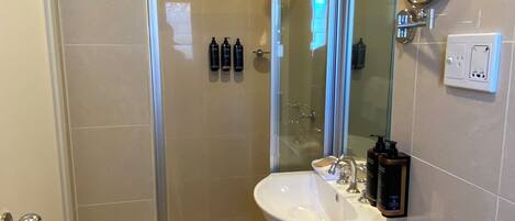 Un baño moderno con cabina de ducha de vidrio, un lavabo blanco y un espejo con marco redondo.