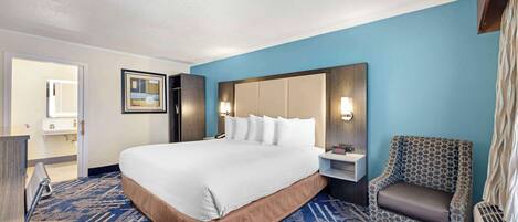 A hotel room with a large bed, a chair, a desk, and a nightstand.