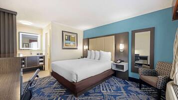 A hotel room with a large bed, a desk with a chair, a mirror, and a blue carpet.