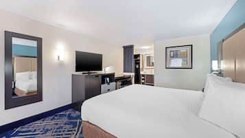 Habitación de hotel con una cama grande, un televisor de pantalla plana, un escritorio con una silla, un espejo y un baño visible a través de una puerta abierta.