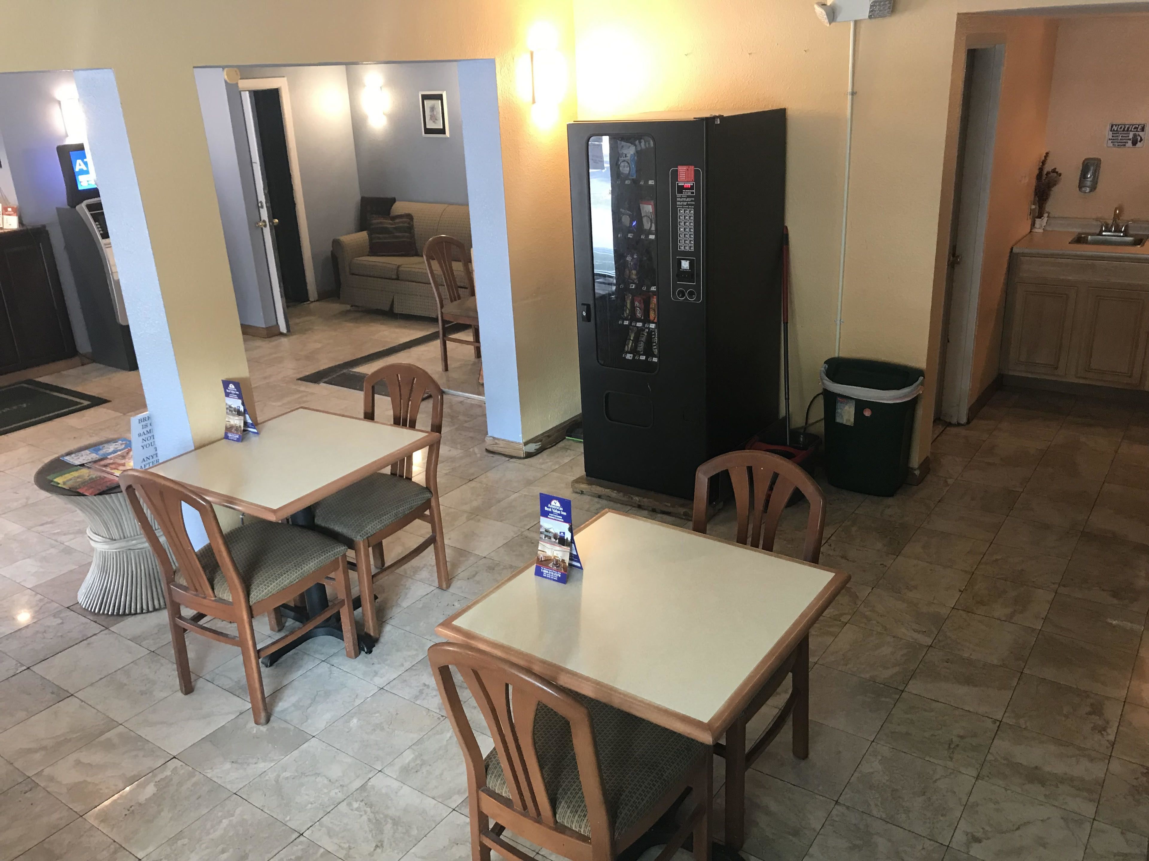 A dining area with two wooden tables and chairs, a refrigerator, and a trash can.