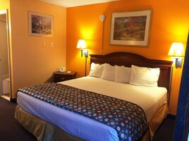 Una habitación de hotel con una cama grande, dos lámparas de noche, un teléfono y dos cuadros en las paredes.