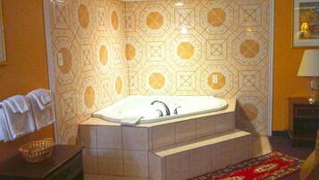 A bathroom with a freestanding bathtub, a towel rack, a small table with a lamp, and a patterned wall.