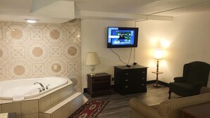 A bathroom with a bathtub, a TV mounted on the wall, a small table with a lamp, and a chair. - Americas Best Value Inn Pottstown (Pottstown)
