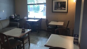 A small inn with a dining area featuring tables and chairs, a sofa, and a window with blinds. - Americas Best Value Inn Pottstown (Pottstown)