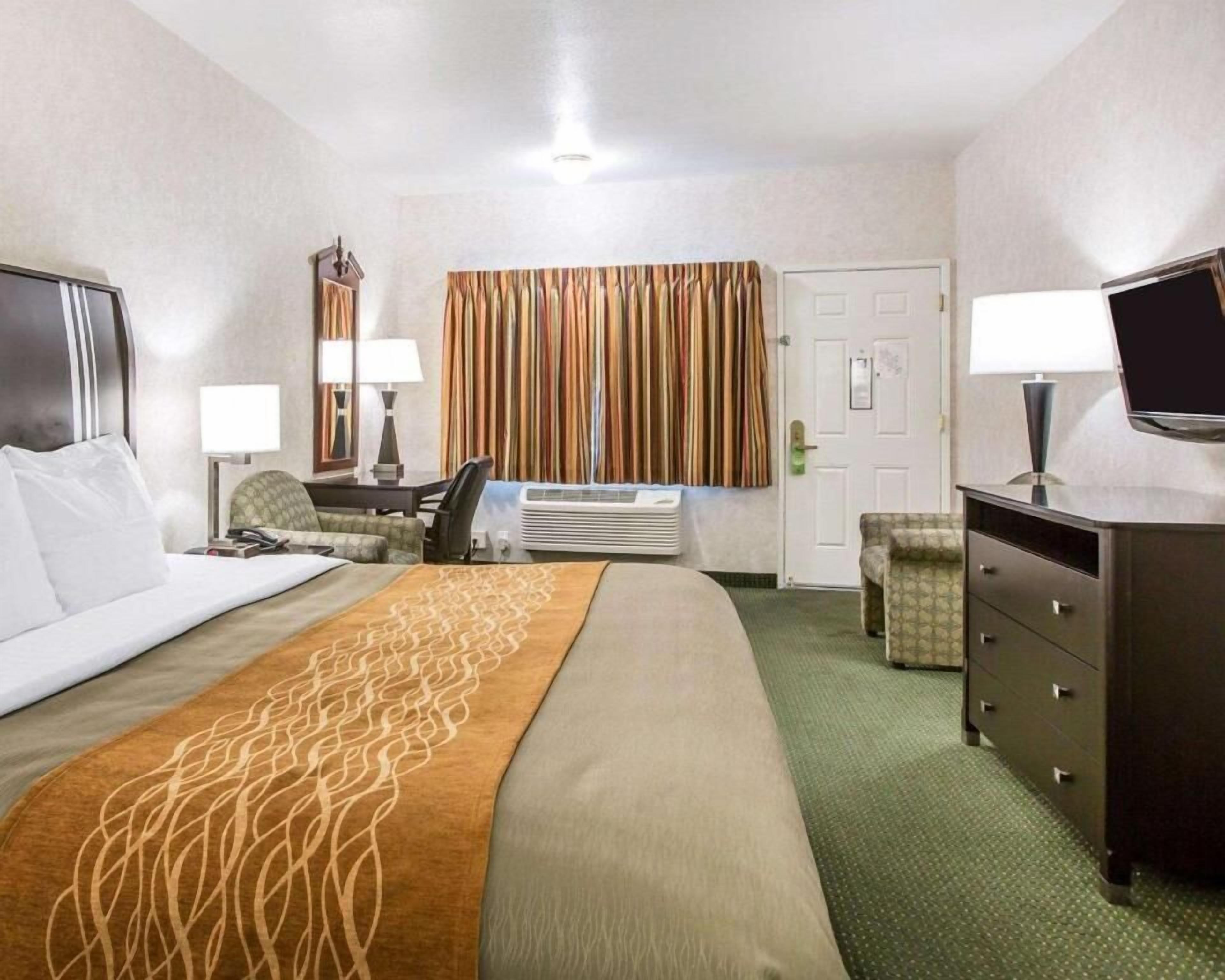 A hotel room with a bed, a desk, a chair, a dresser, and a television.