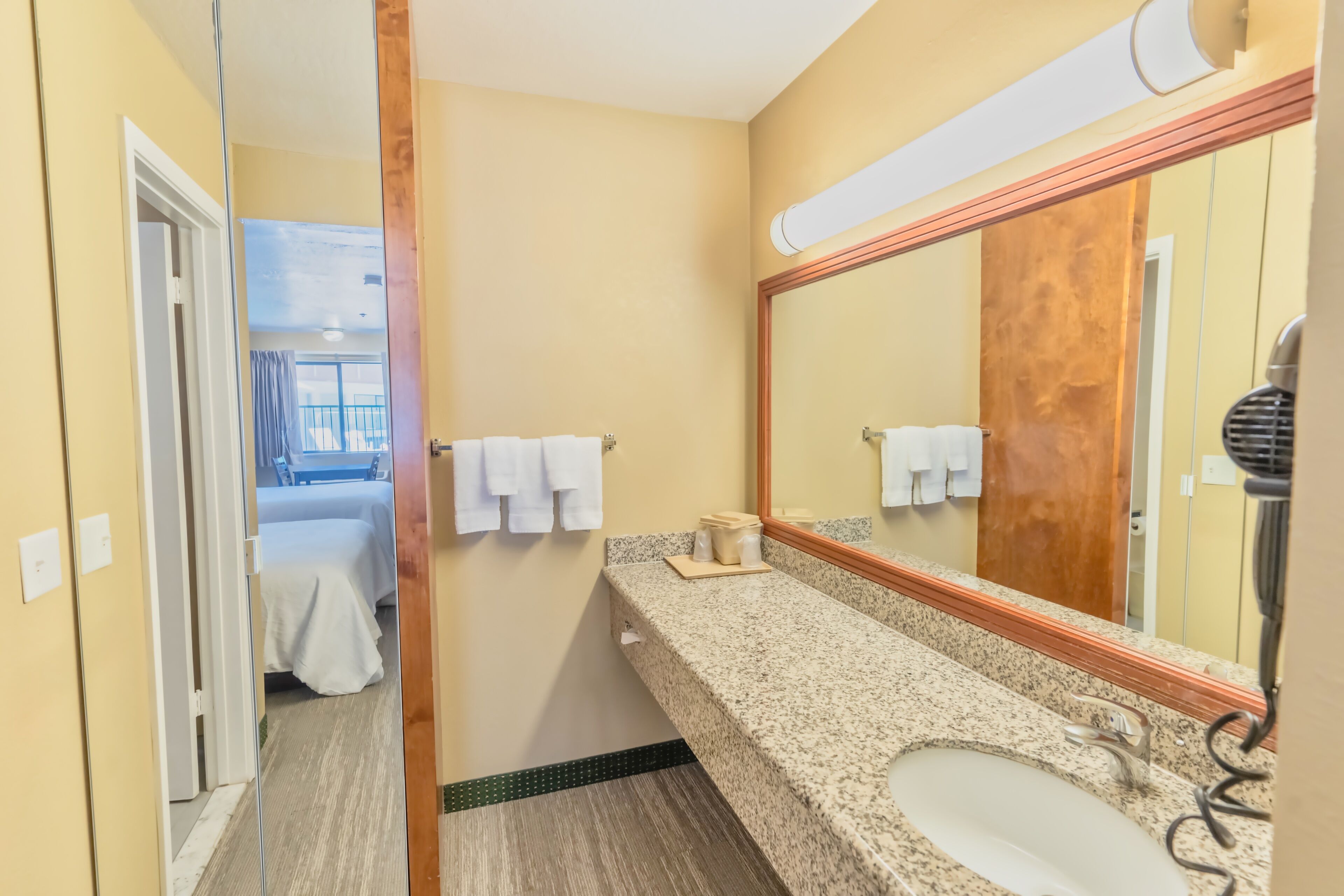 A hotel bathroom with a granite countertop, a sink, a mirror, and a towel rack.