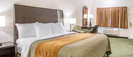 Habitación de hotel con una cama grande, un escritorio, una silla, una lámpara y una ventana con cortinas.