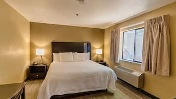 A hotel room with a large bed, two bedside lamps, a window with curtains, and a wall-mounted air conditioner.