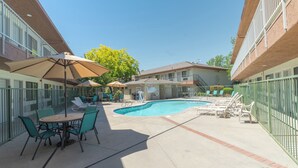 Ein Poolbereich mit Liegestühlen und Sonnenschirmen, umgeben von einem Ziegelgebäude mit einem Balkon.
