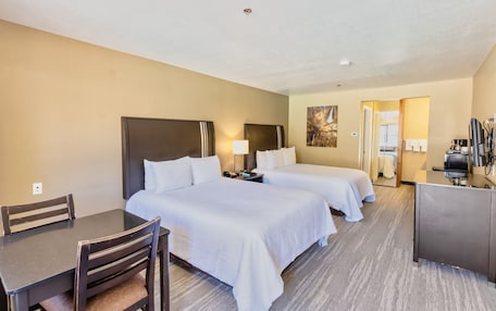 A hotel room with two beds, a desk, a chair, a TV, and a kitchenette.