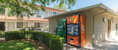 Un edificio con una máquina expendedora verde, un seto y un cielo despejado.