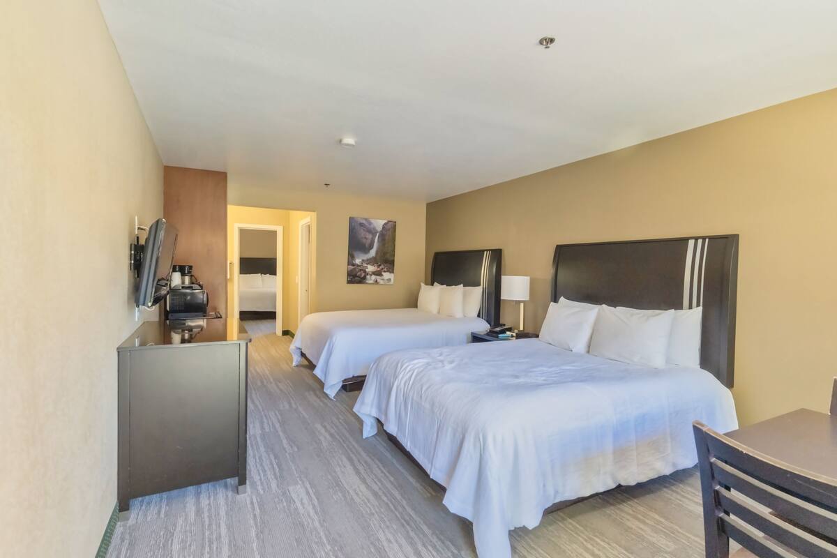 A hotel room with two beds, a desk, a chair, a TV, and a painting on the wall.