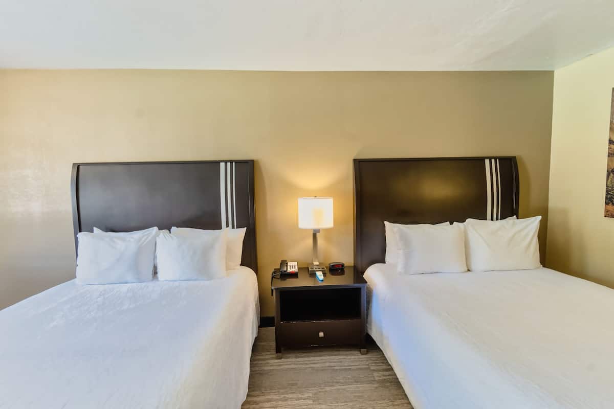 A hotel room with two single beds, a nightstand with a lamp, and a small table with a phone and a remote control.