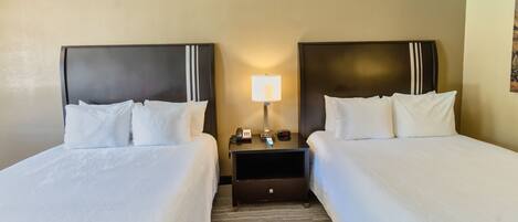 A hotel room with two single beds, a nightstand with a lamp, and a small table with a phone and a remote control.