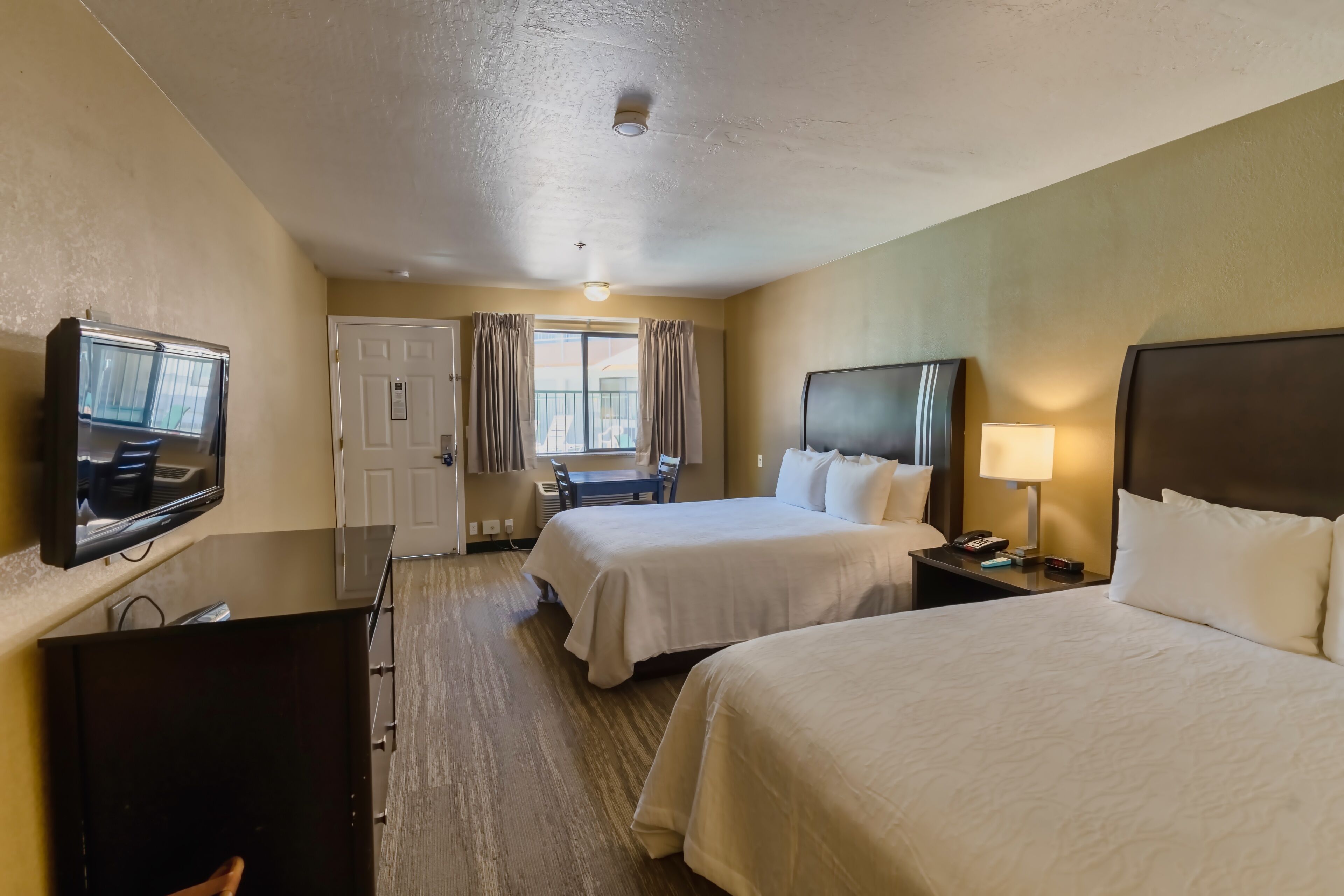 A hotel room with two beds, a TV, a desk, and a window with curtains.