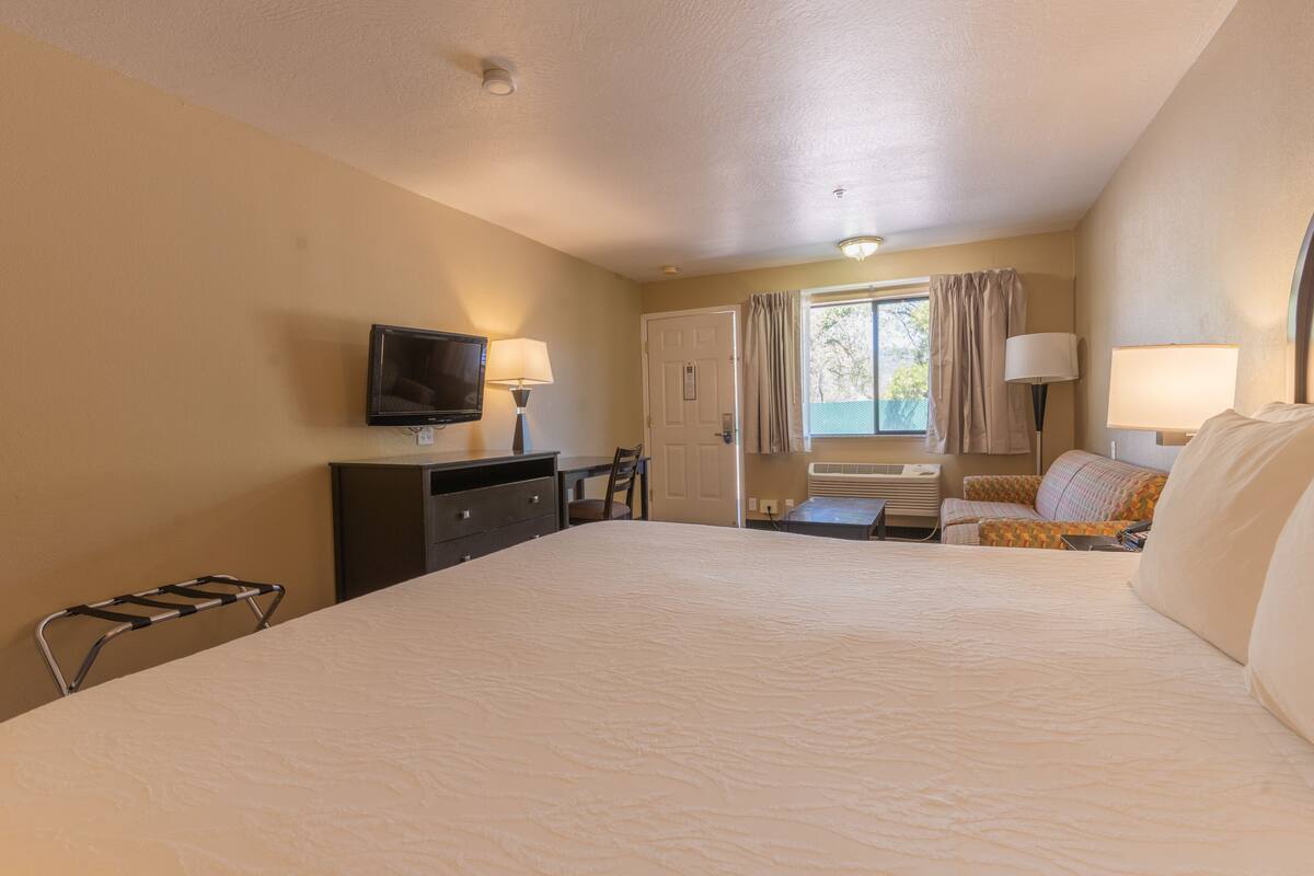 A hotel room with a large bed, a desk, a chair, a television, and a window with curtains.
