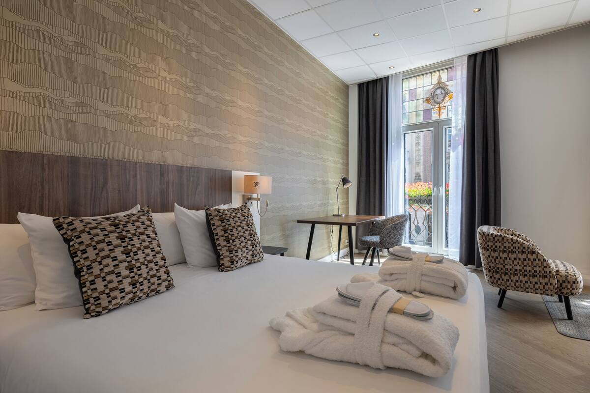 A hotel room with a large bed, a desk, a chair, and a view of the outdoors.