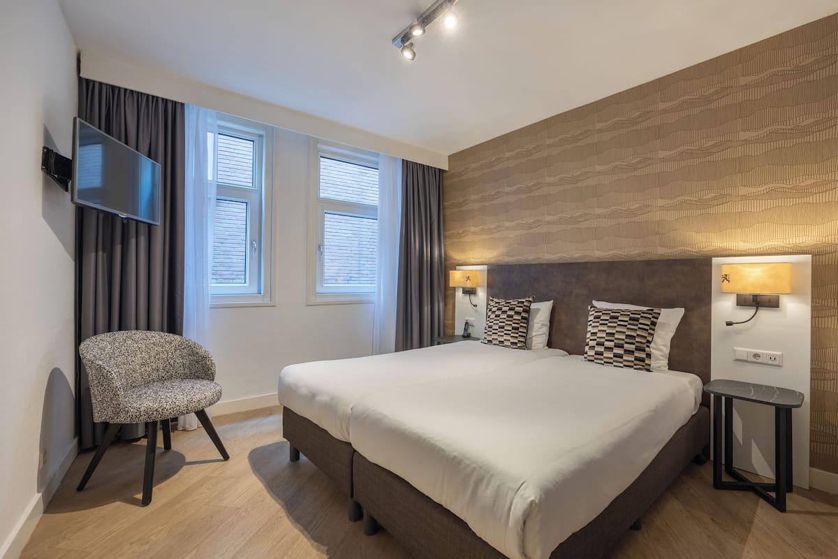 A modern hotel room with a large bed, a television mounted on the wall, and a desk with a lamp.