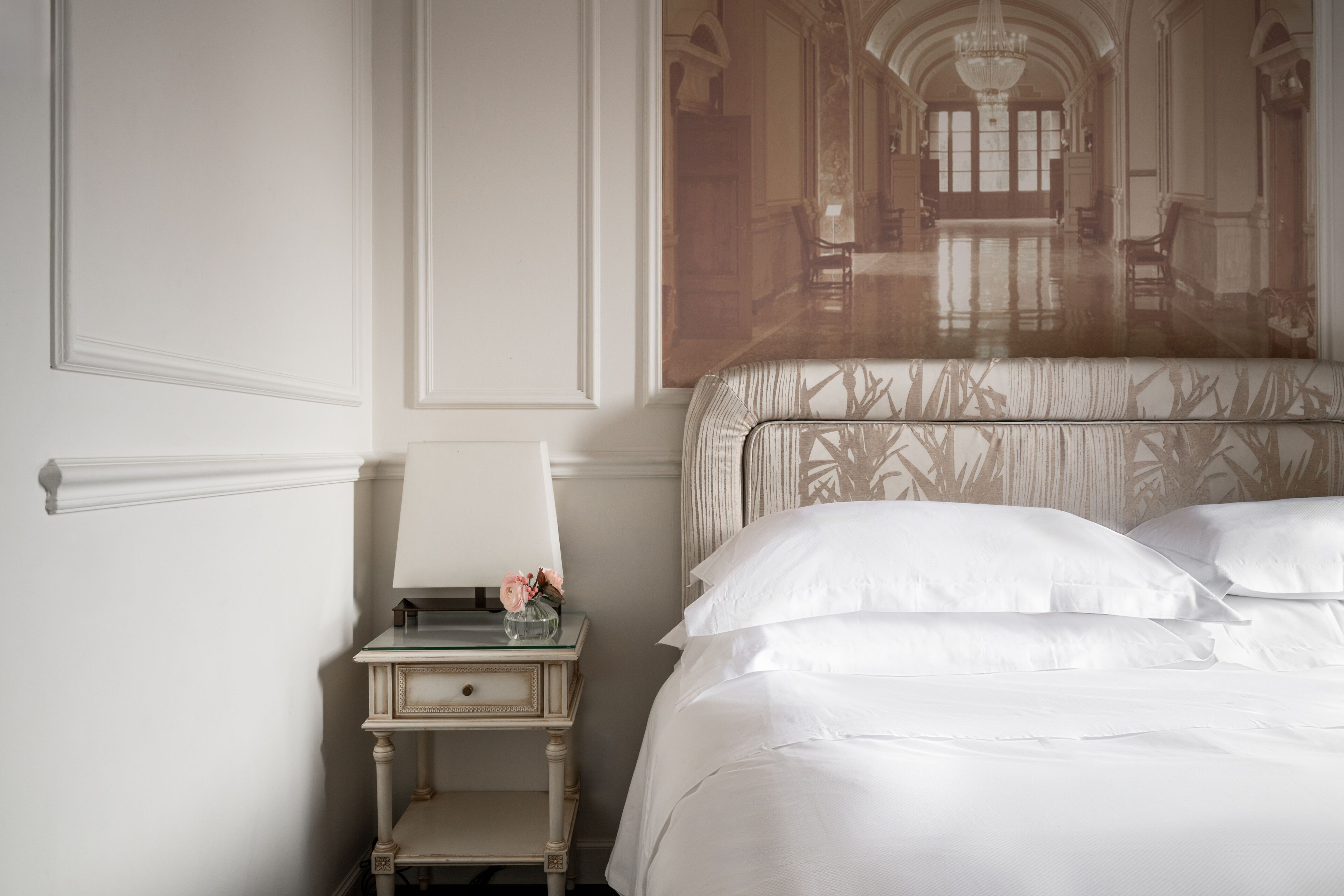 A bedroom with a bed, a nightstand with a lamp, and a mirror.