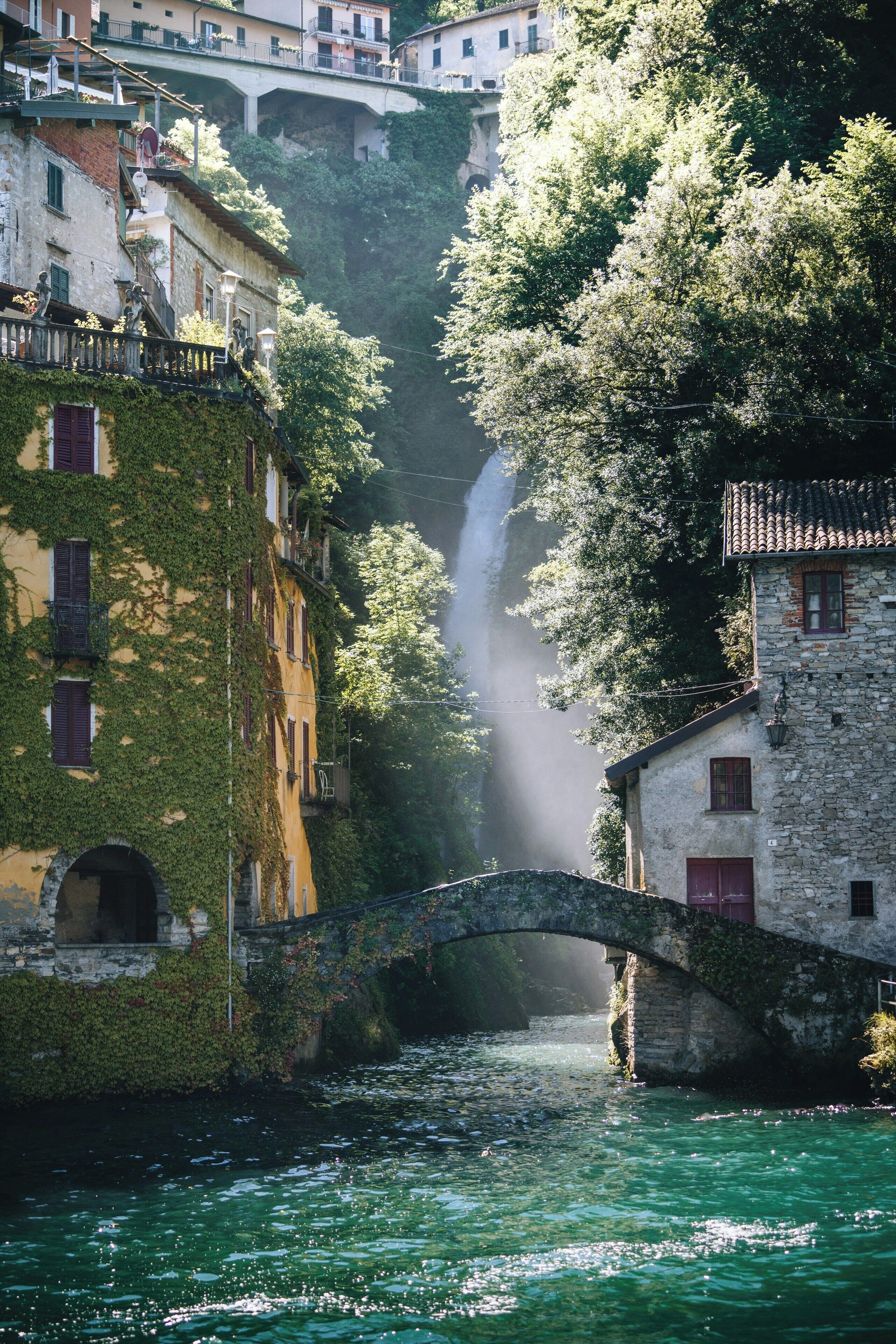 A stone bridge over a river with buildings on either side, including a building with ivy-covered walls and another with a stone facade.