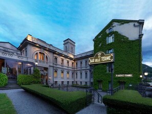 Un edificio histórico con el cartel de Bar delle Terme, que presenta arquitectura clásica y un jardín bien cuidado.
