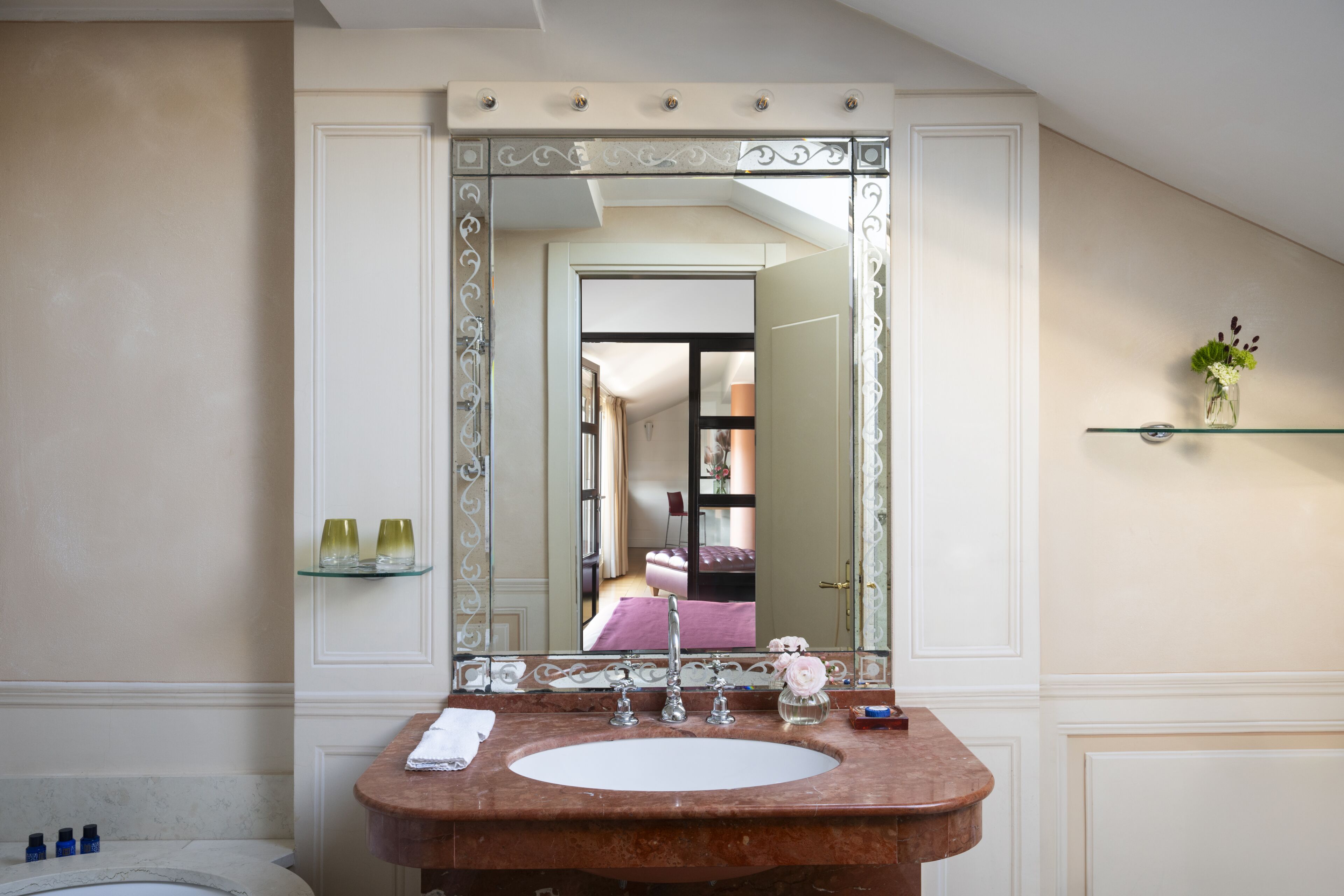 A bathroom with a large mirror, a marble sink, and a glass shelf with toiletries.
