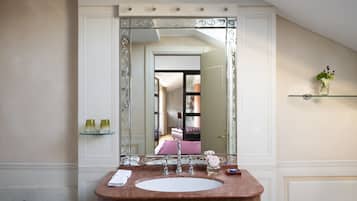 A bathroom with a large mirror, a marble sink, and a glass shelf with toiletries.