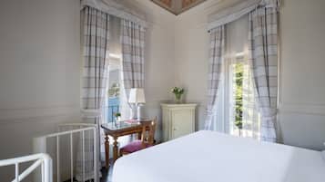 Una habitación de hotel con una cama, un escritorio con lámpara, una silla, un armario y cortinas.