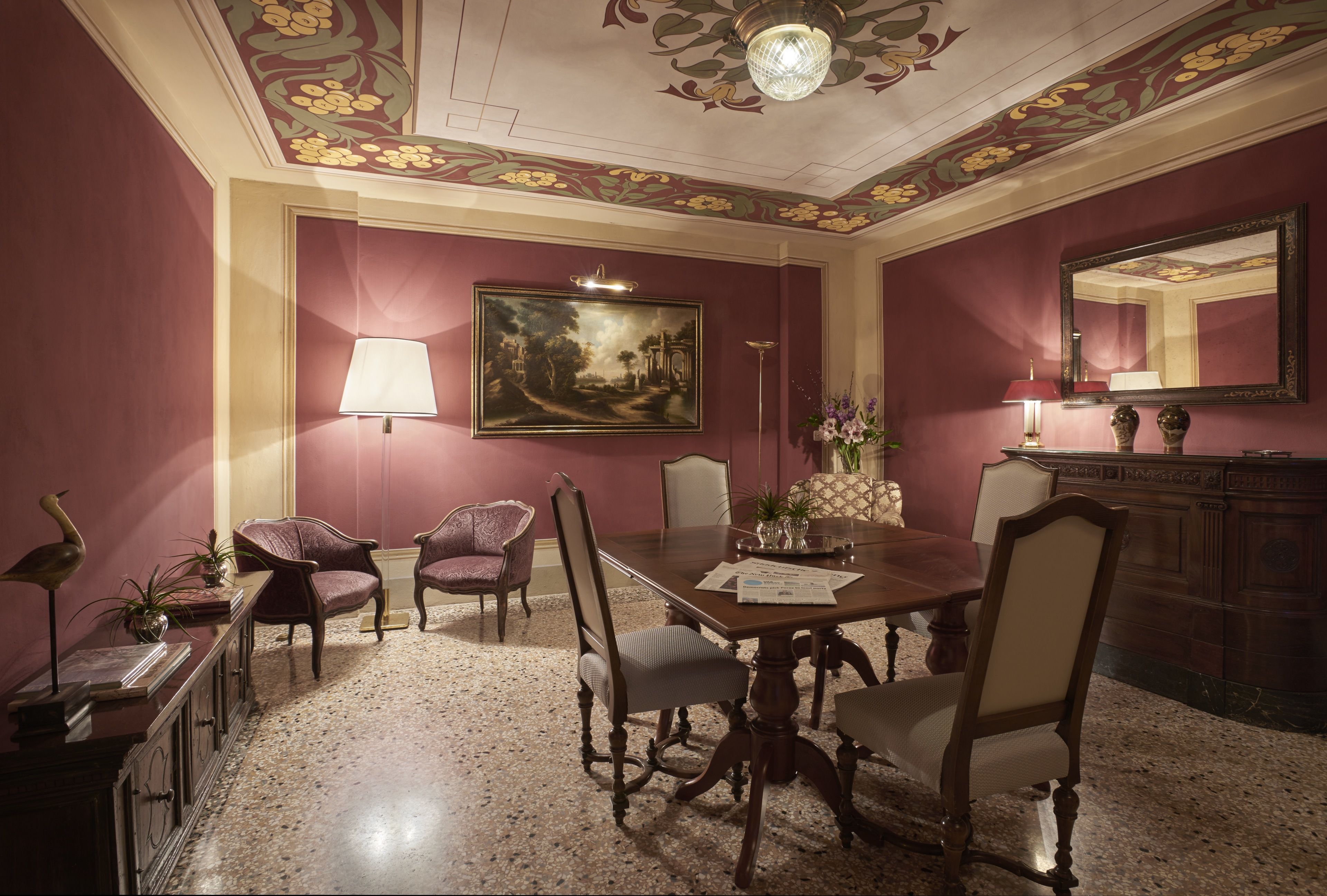 Una sala de dinar formal amb una taula gran, cadires, un penjador de cristall i un quadre a la paret.