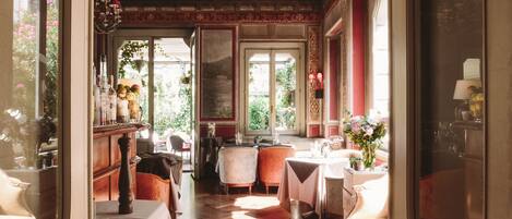 A dining area with a wooden parquet floor, tables set for dining, and a view of the garden through large windows.