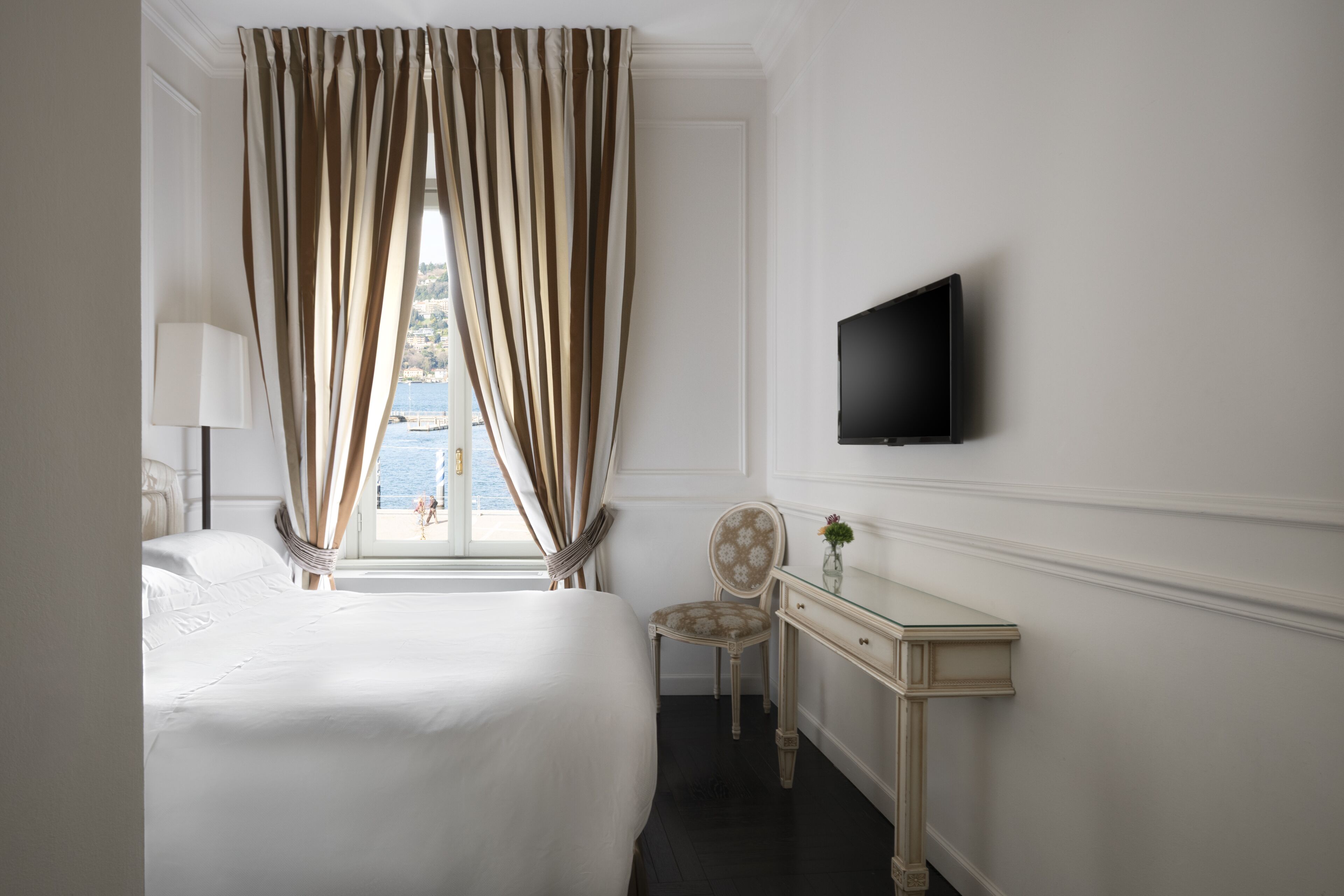 Een hotelkamer met een bed, een bureau, een stoel, een televisie en een raam met gordijnen.