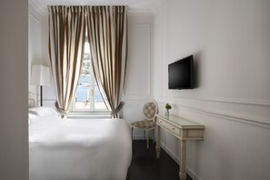 A hotel room with a bed, a desk, a chair, a TV, and a window with curtains. - Albergo Terminus Hotel (Como)