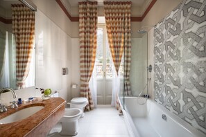 A bathroom with a marble sink, two toilets, a bathtub, and patterned shower walls. - Albergo Terminus Hotel (Como)