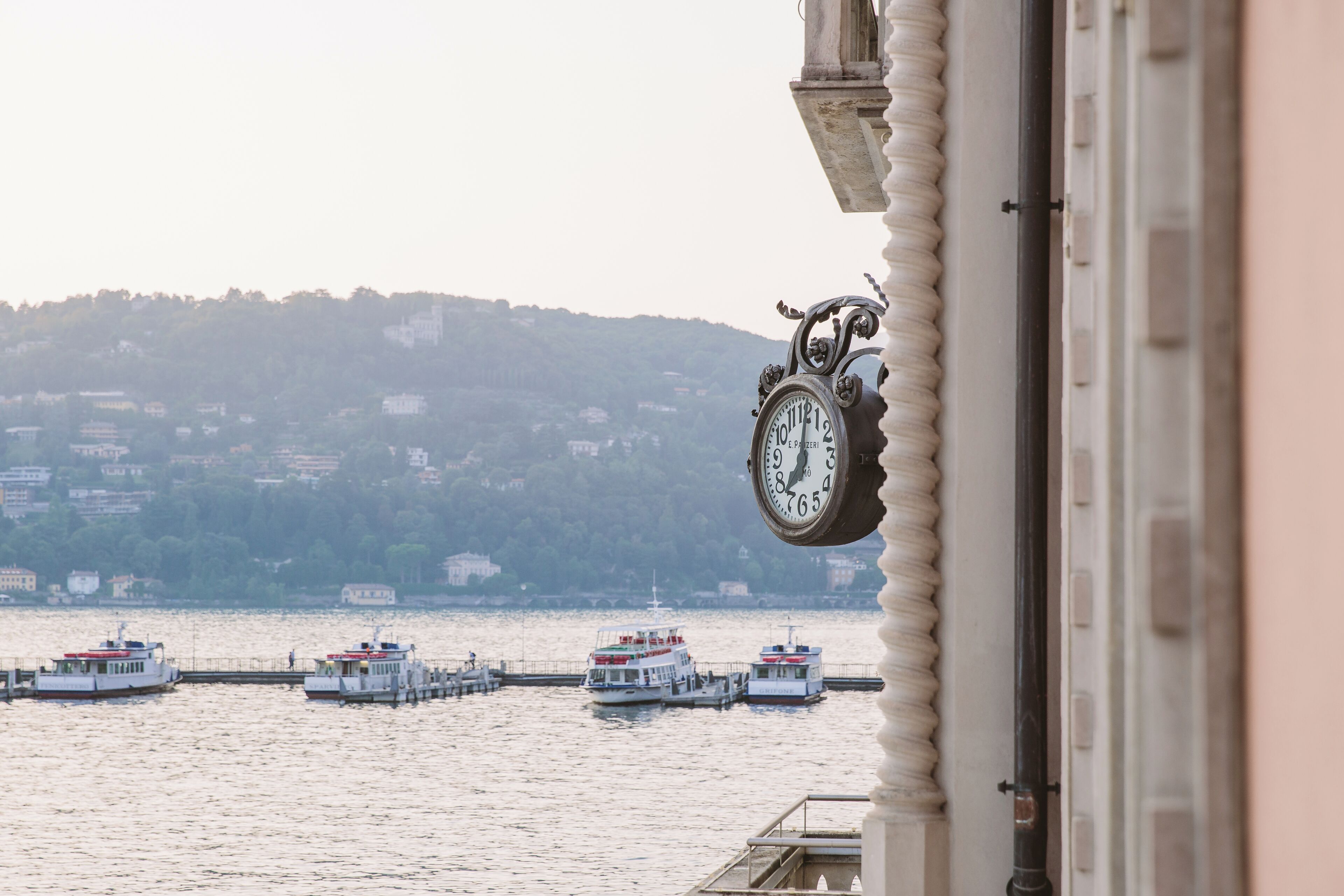 Un reloj con vistas a barcos en el agua y un paisaje montañoso al fondo.